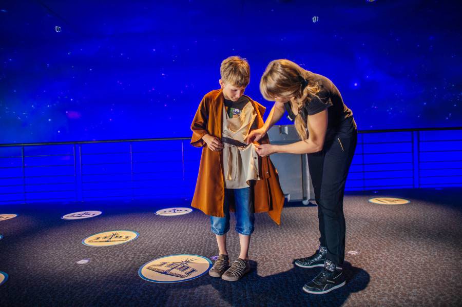 A Padawan is being fit in a Jedi Tunic by a Cast Member.